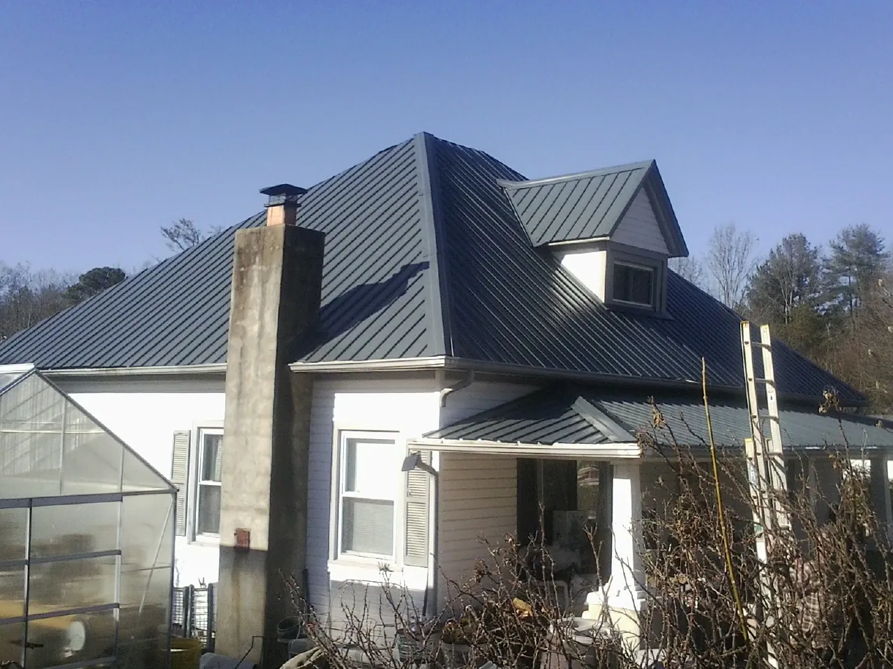 Dark blue standing seam metal roof on a white farmhouse with dormer — Slate & Tile Roof Repair by Roofing Brothers in Madera