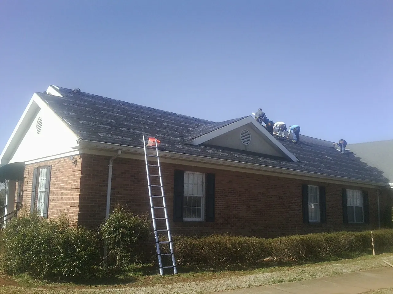 Crew tearing shingles off a brick ranch roof with a ladder set — Metal Roof Repair work by our crew in Madera