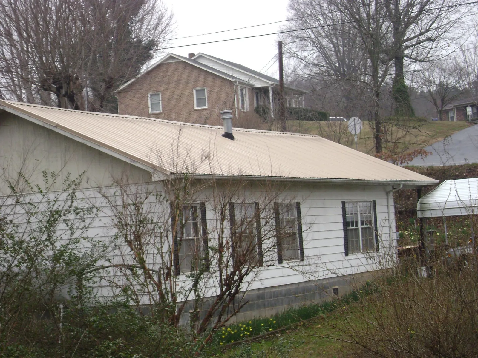 Tan metal roof on a white sided house set into a hillside — Commercial Roofing by Roofing Brothers in Madera