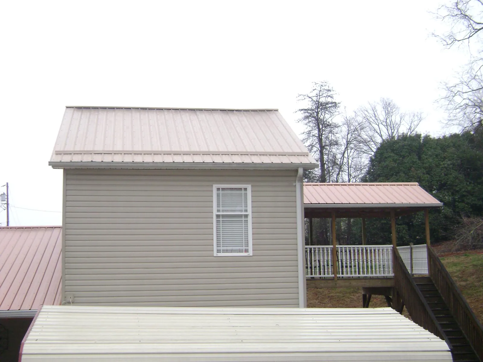 Tan metal roofs on a two story addition and attached porch, from a Roof Replacement job in Madera